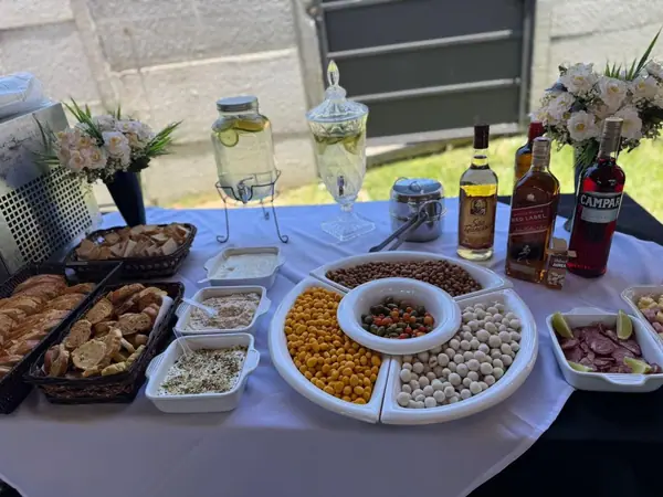 Mesa de petiscos e jarras de bebida sobre toalha branca