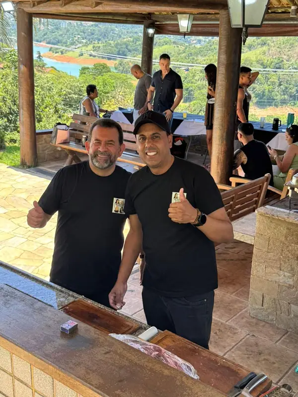 Dois integrantes da equipe sorrindo ao lado da churrasqueira